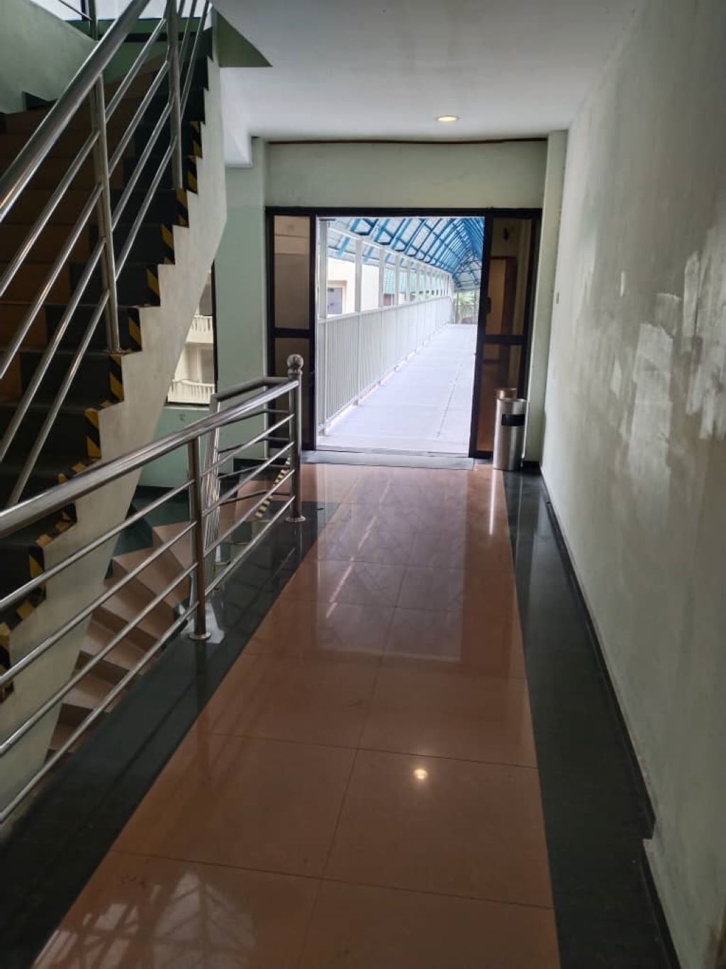 Un pasillo con una escalera a la izquierda, un techo de cristal a la derecha y una puerta al final.