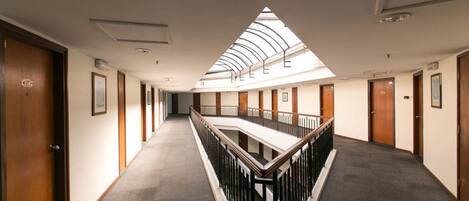 A hotel corridor with a skylight, wooden doors, and a central railing.