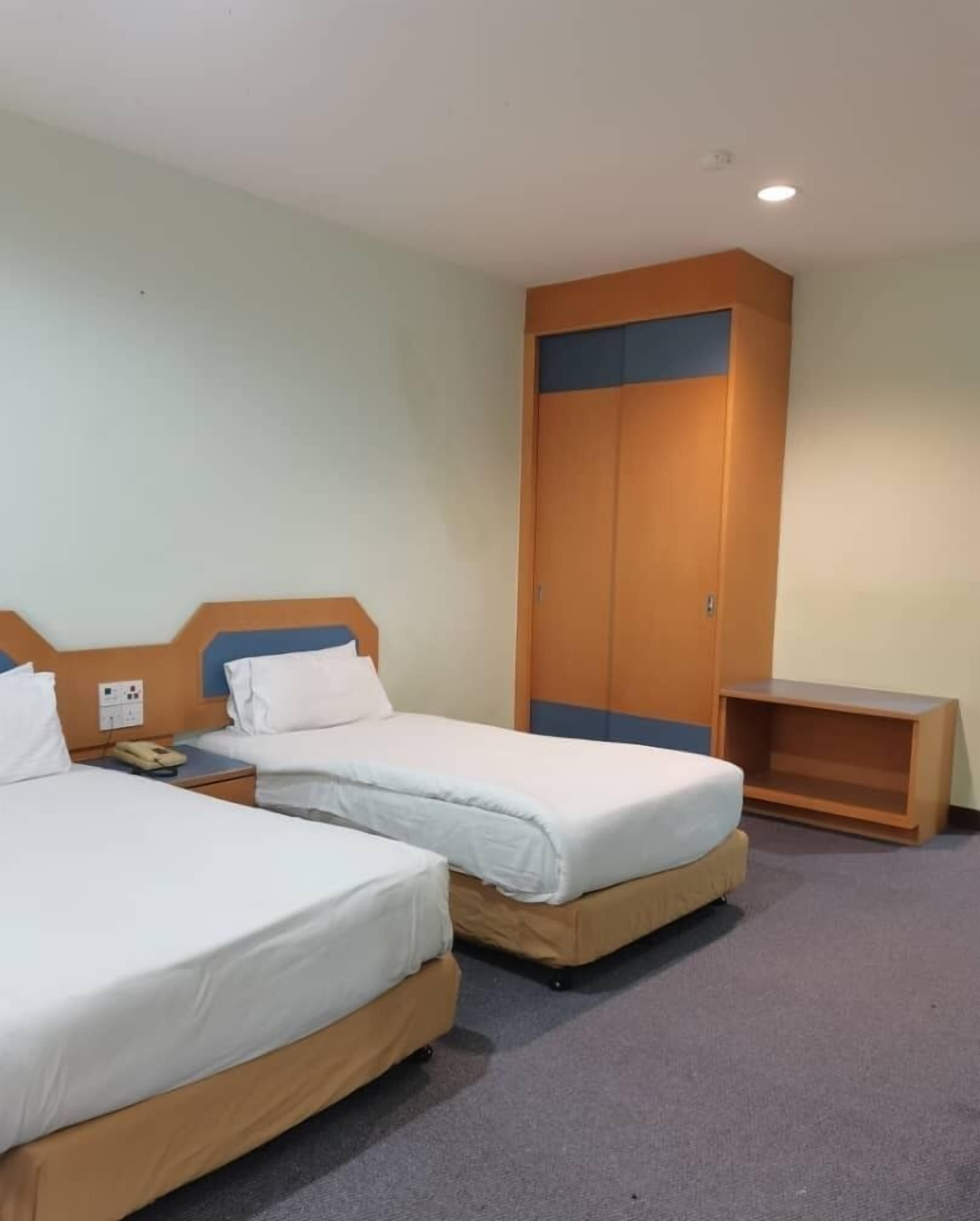A hotel room with two single beds, a wooden wardrobe, a small table, and a telephone on the nightstand.