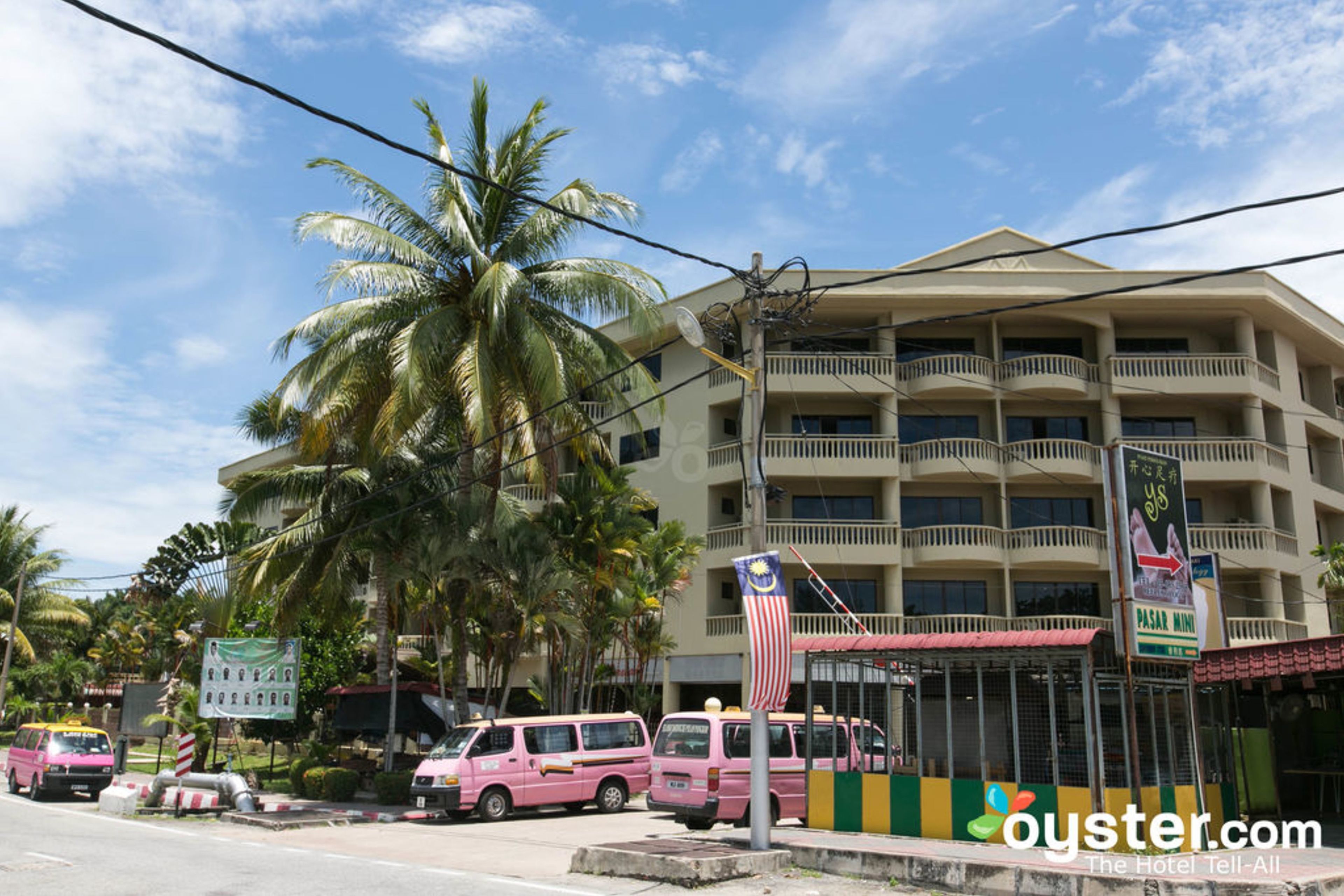 A multi-story hotel with balconies, palm trees, and a sign for a Pasar Mini.