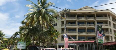 A multi-story hotel with balconies, palm trees, and a sign for a Pasar Mini.