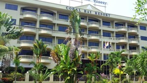 Ein mehrstöckiges Hotel namens Coral Bay Resort mit Balkonen und üppiger tropischer Bepflanzung.
