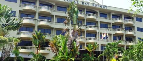 Ein mehrstöckiges Hotel namens Coral Bay Resort mit Balkonen und üppiger tropischer Bepflanzung.