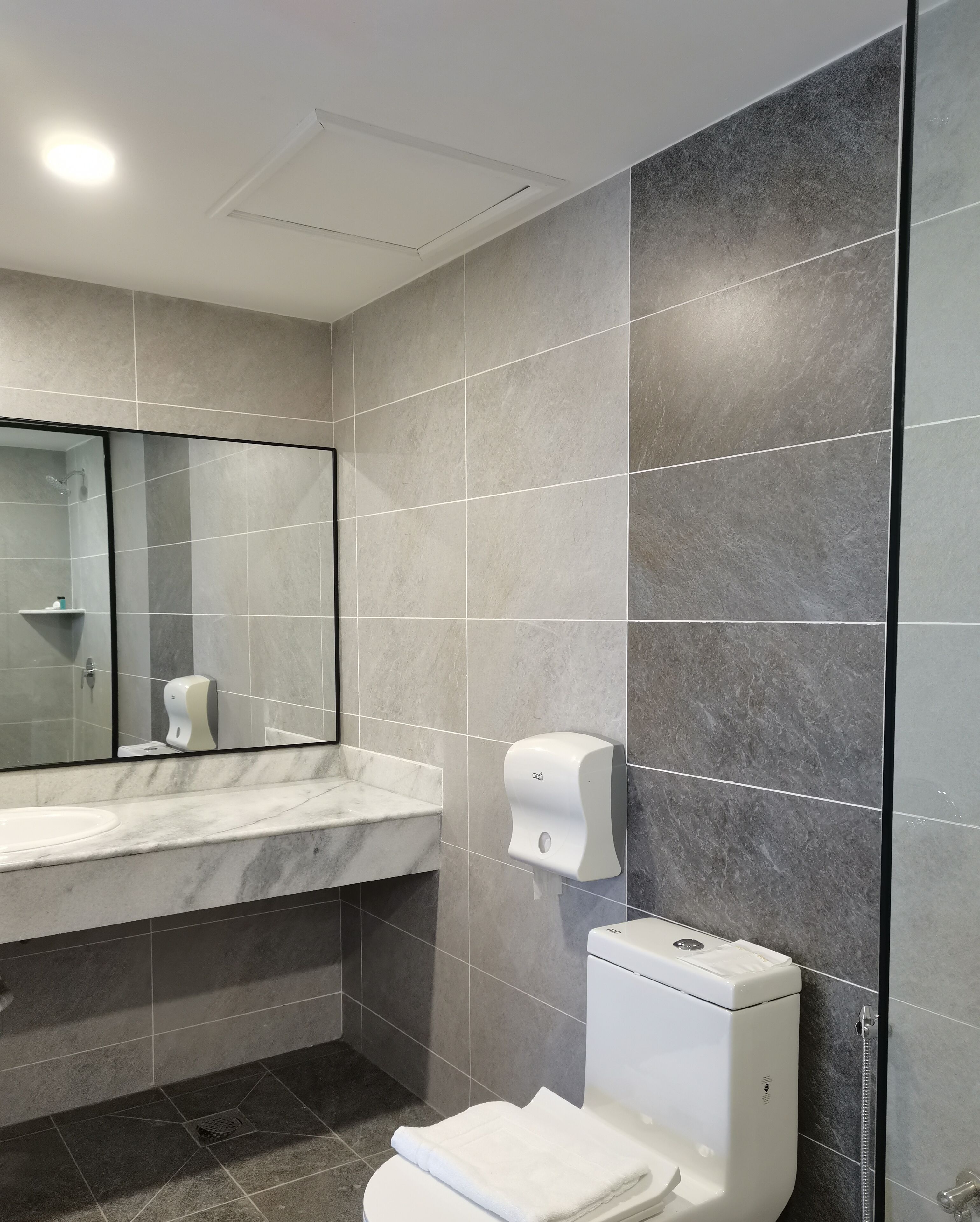 A modern bathroom with a marble sink, a hand soap dispenser, a toilet, and a mirror.