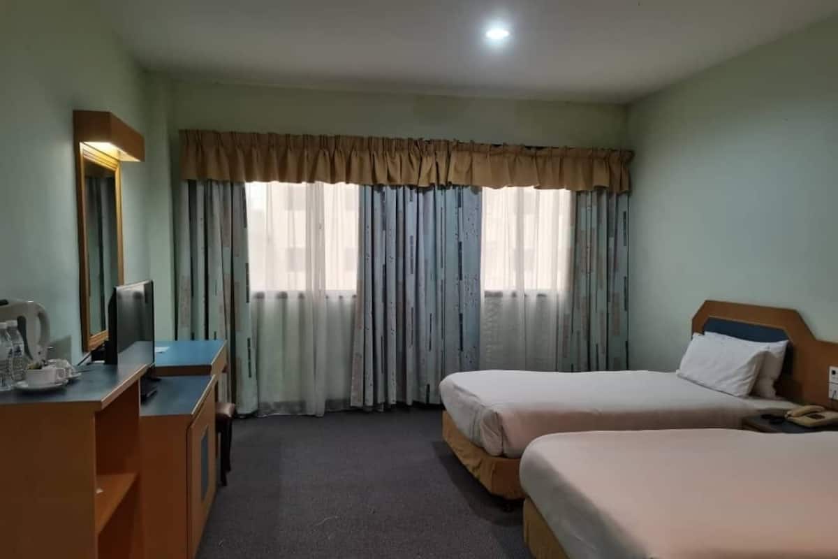 Habitación de hotel con dos camas, un escritorio con ordenador, un espejo y una ventana con cortinas.
