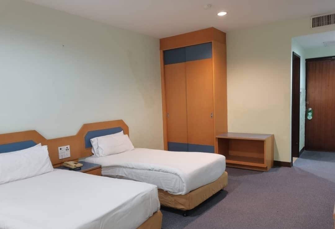A hotel room with two beds, a wardrobe, a bedside table, and a door.