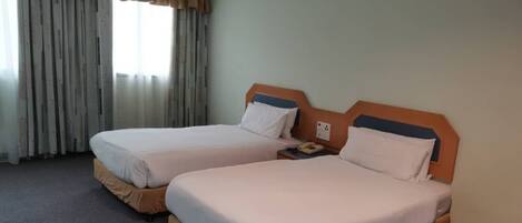 Una habitación de hotel con dos camas, una ventana con cortinas y un teléfono en la mesita de noche.