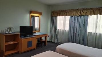 A hotel room with a desk, television, and two beds.