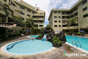 A hotel pool area with two swimming pools, palm trees, and a waterfall.