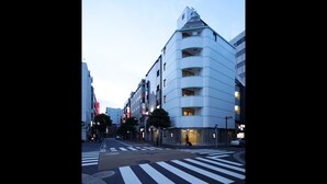 A modern urban street with a distinctive corner building featuring a unique triangular top and multiple balconies. - ℃ (Do-C) Gotanda (Tokyo)
