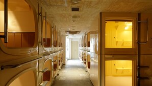 A narrow corridor with bunk beds on either side and a central passageway leading to a door. - ℃ (Do-C) Gotanda (Tokyo)