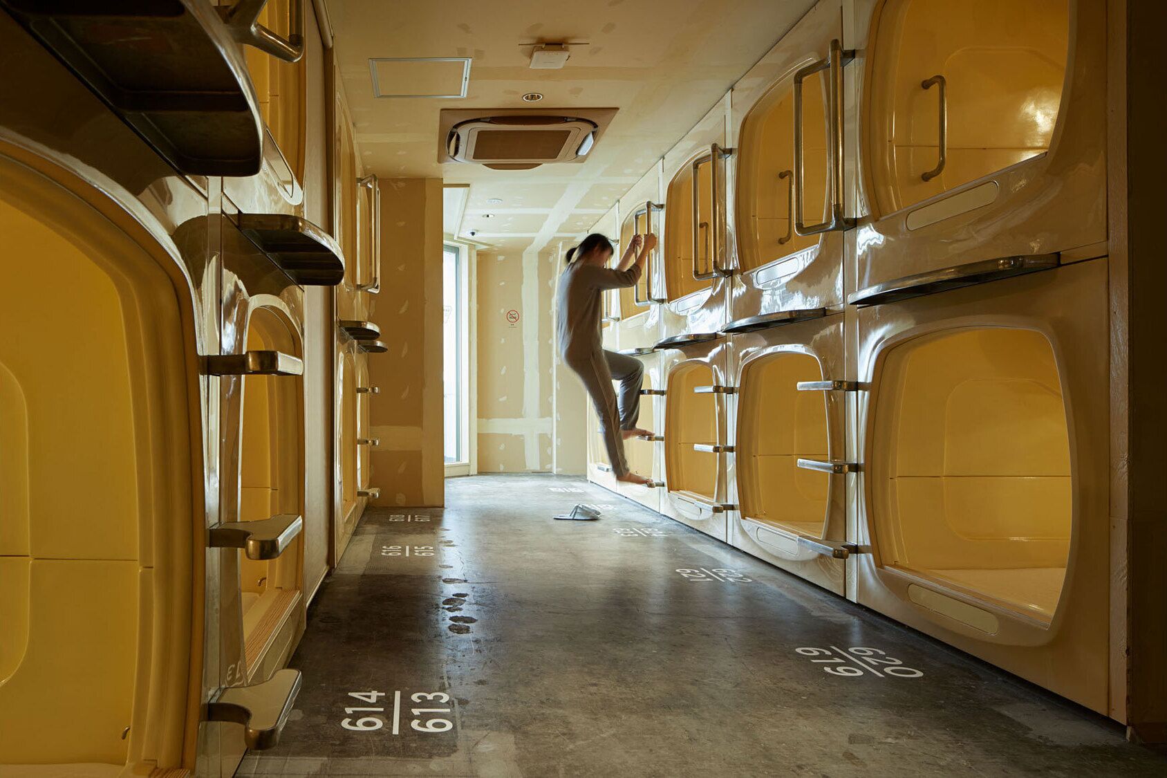 A narrow hallway with yellow lockers and a person climbing a ladder.