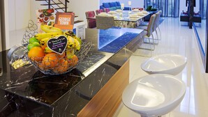 Een hotel receptie met een marmeren balie, een fruitmand en een zithoek met een blauwe bank en een eettafel.