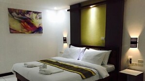 A neatly made bed with white linens and a decorative headboard, a small bedside table, and a wall-mounted light fixture. - Ark Bayz Suites (Puerto Galera)
