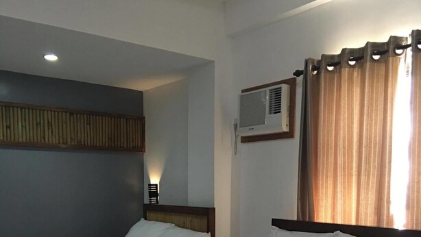 A hotel room with two beds, a wooden headboard, a wall-mounted air conditioner, and a curtain. - Ark Bayz Suites (Puerto Galera)