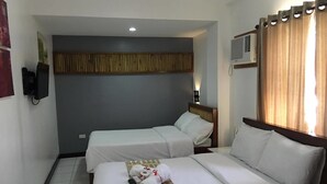 A hotel room with two single beds, a wooden headboard, a wall-mounted air conditioner, and a small TV. - Ark Bayz Suites (Puerto Galera)