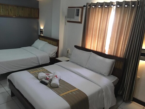 Habitación de hotel con dos camas individuales, una mesita de noche con lámpara, una ventana con cortinas y un aire acondicionado instalado en la pared.