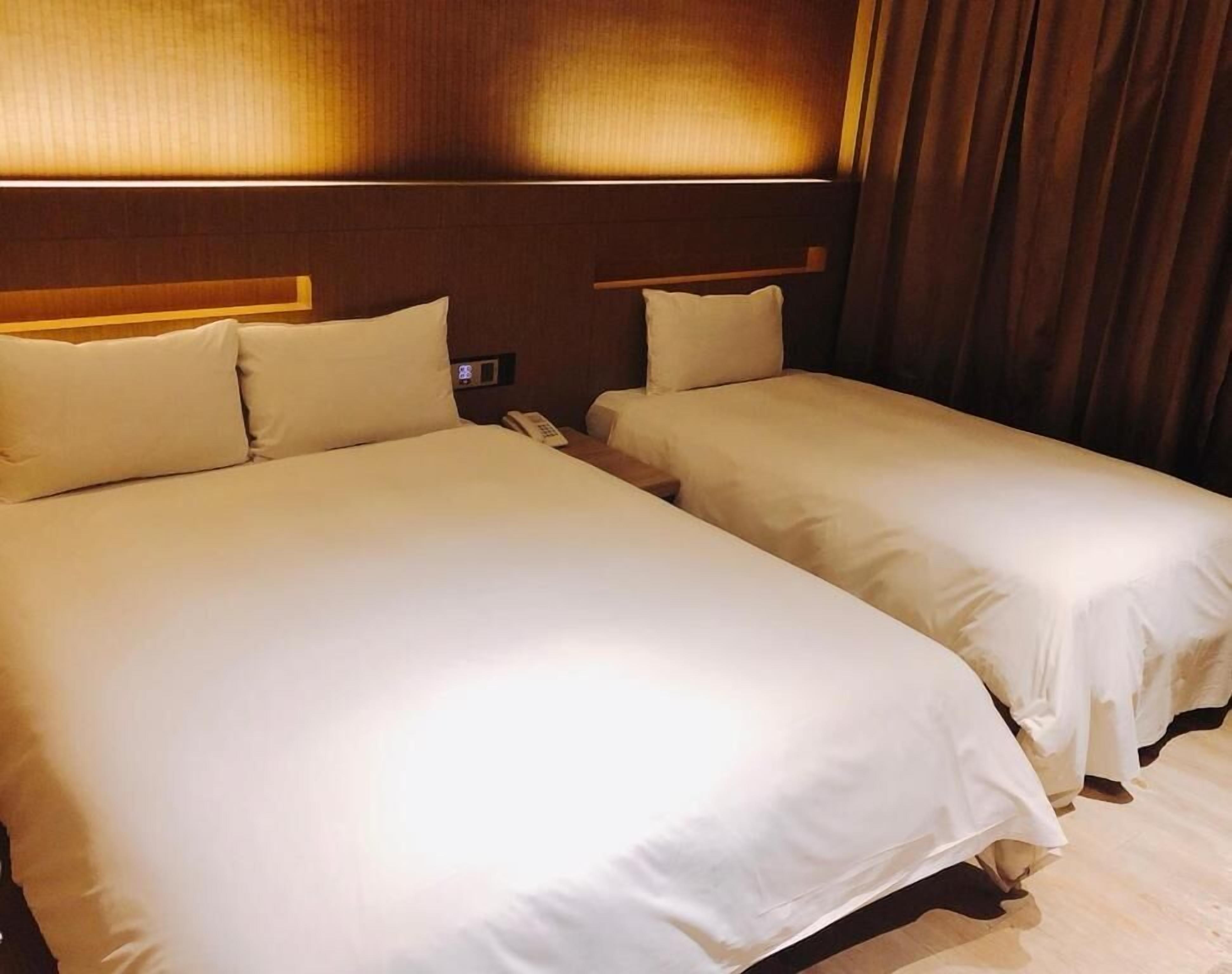 A hotel room with two beds, a wooden headboard, a bedside telephone, and a curtain.