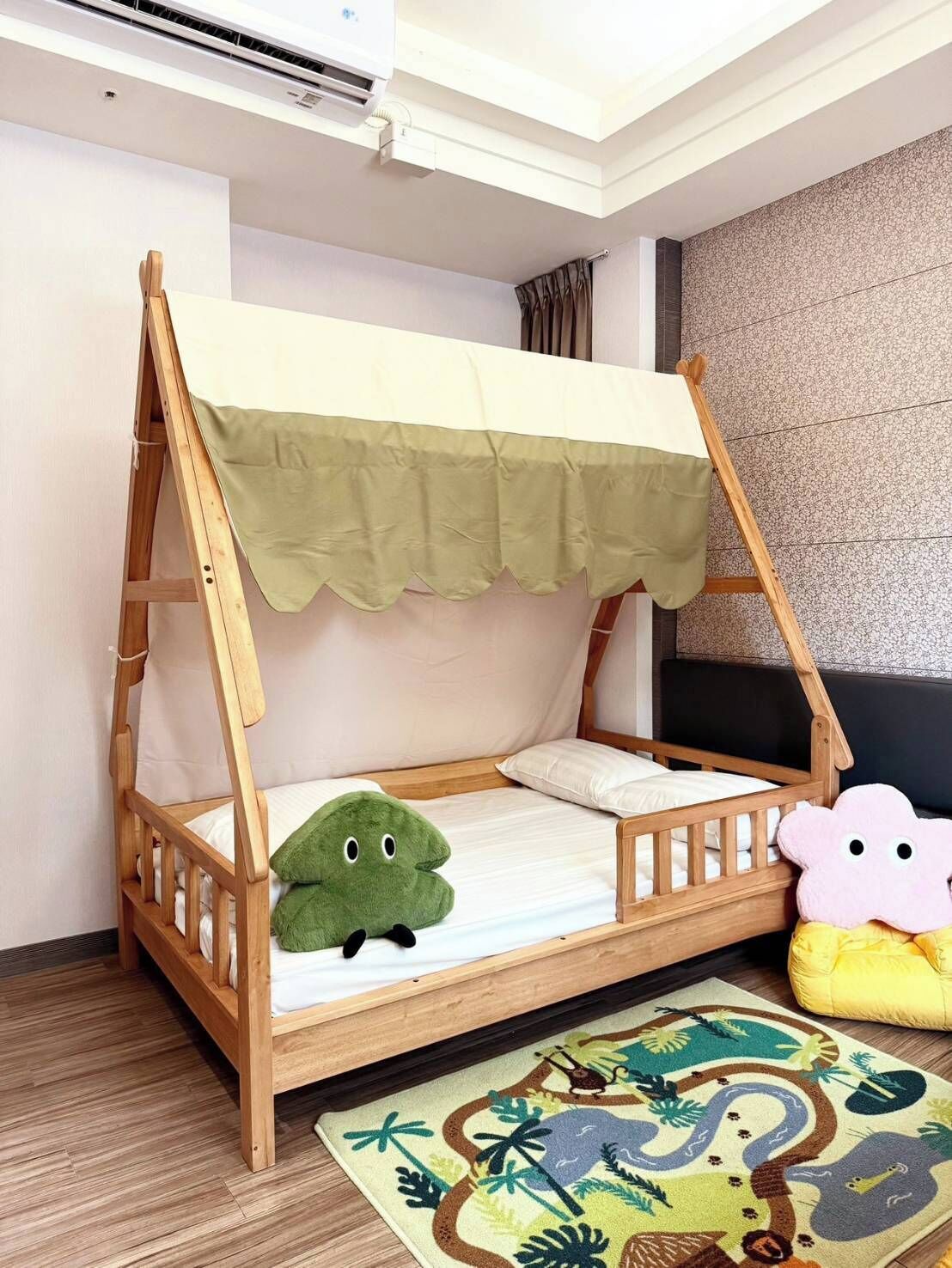 Una cama litera de madera con dosel, un peluche verde, un peluche rosa y una alfombra estampada.