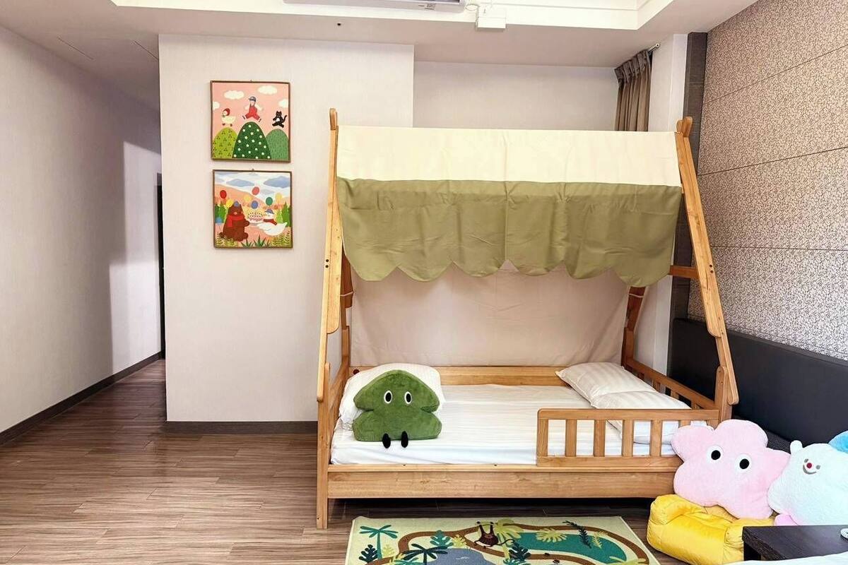 A child-sized bed with a green canopy, a wooden headboard, and a plush green dinosaur pillow.