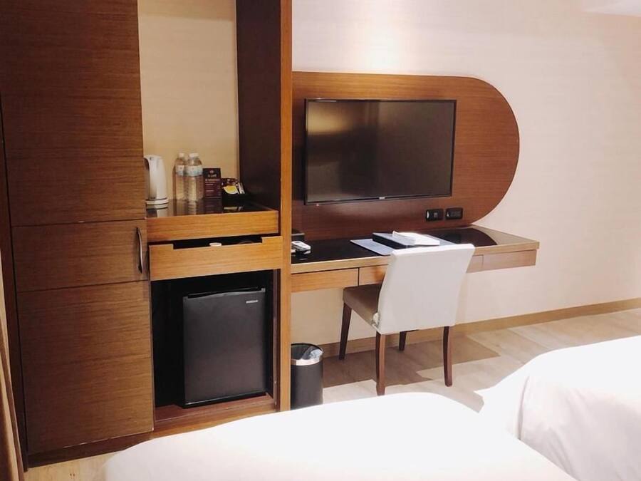 A hotel room with a wooden desk, a television, a small refrigerator, a chair, and a bed.