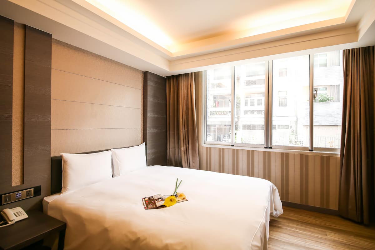 A hotel room with a large bed, a bedside table with a phone, and a window with curtains.