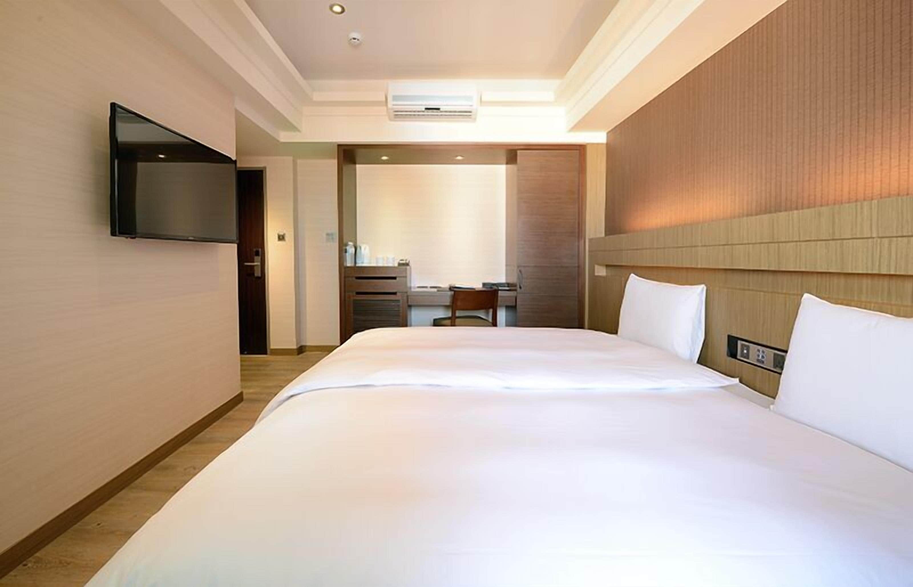 A hotel room with a large bed, a flat-screen TV mounted on the wall, a desk with a chair, and a mirror.