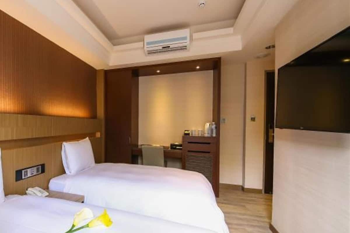 A hotel room with two beds, a desk, a chair, a TV, and a bathroom.