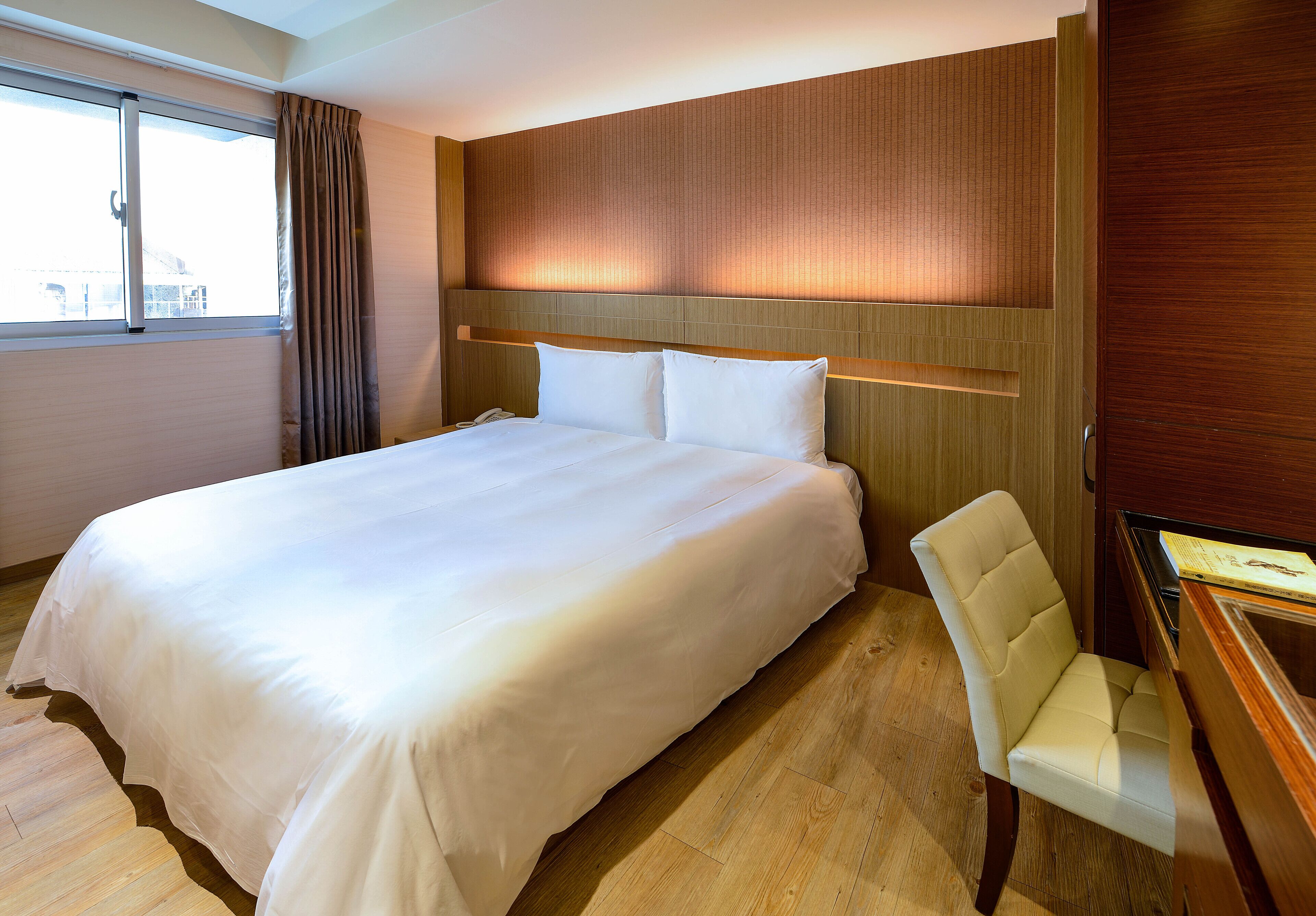Een hotelkamer met een groot bed, een houten hoofdbord, een witte stoel en een bureau met een lamp.