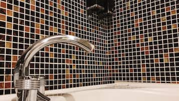 Un baño con grifo cromado, lavamanos blanco y pared de mosaicos.