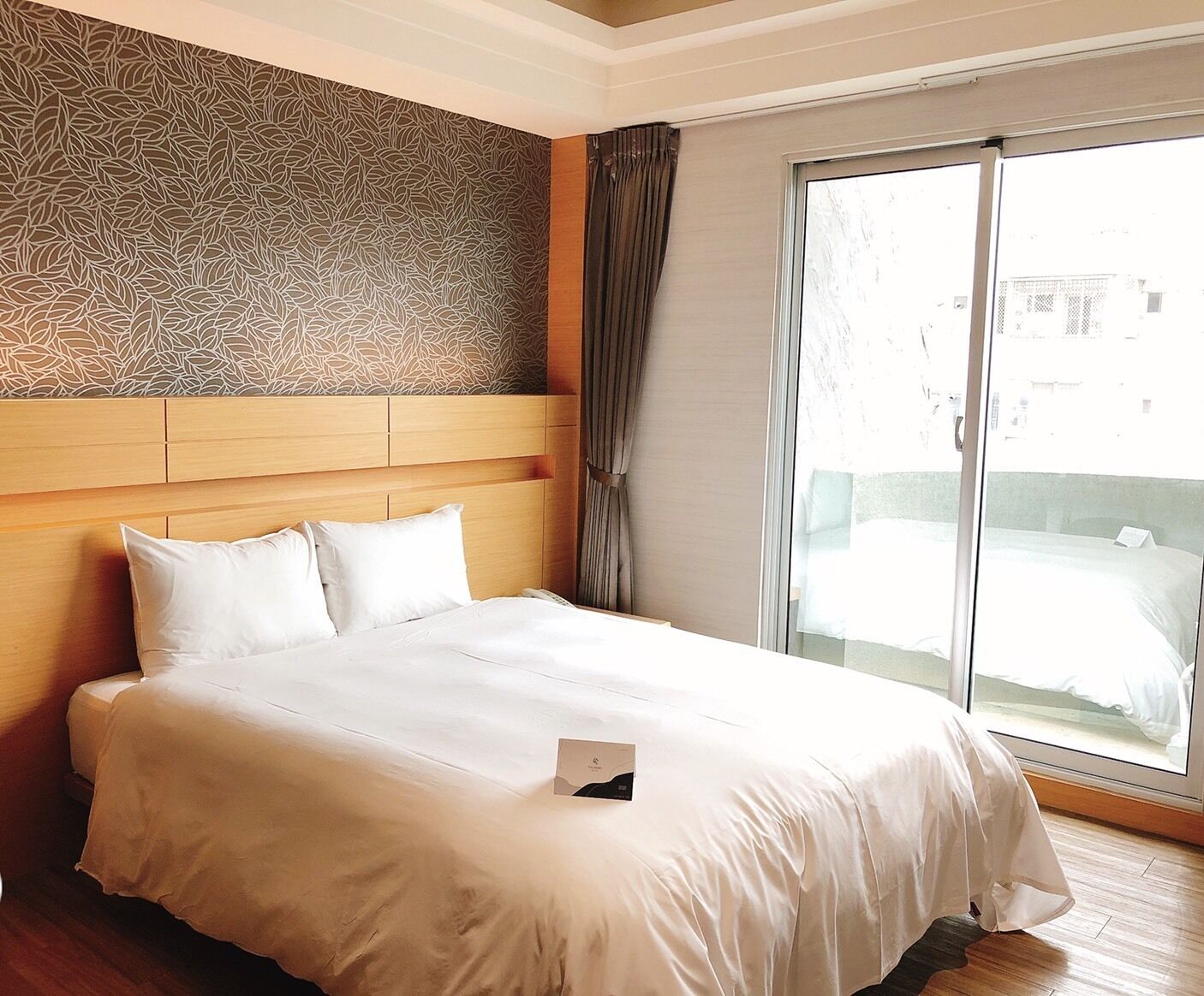 A hotel room with a large bed, a patterned wall, and a view through a sliding door.