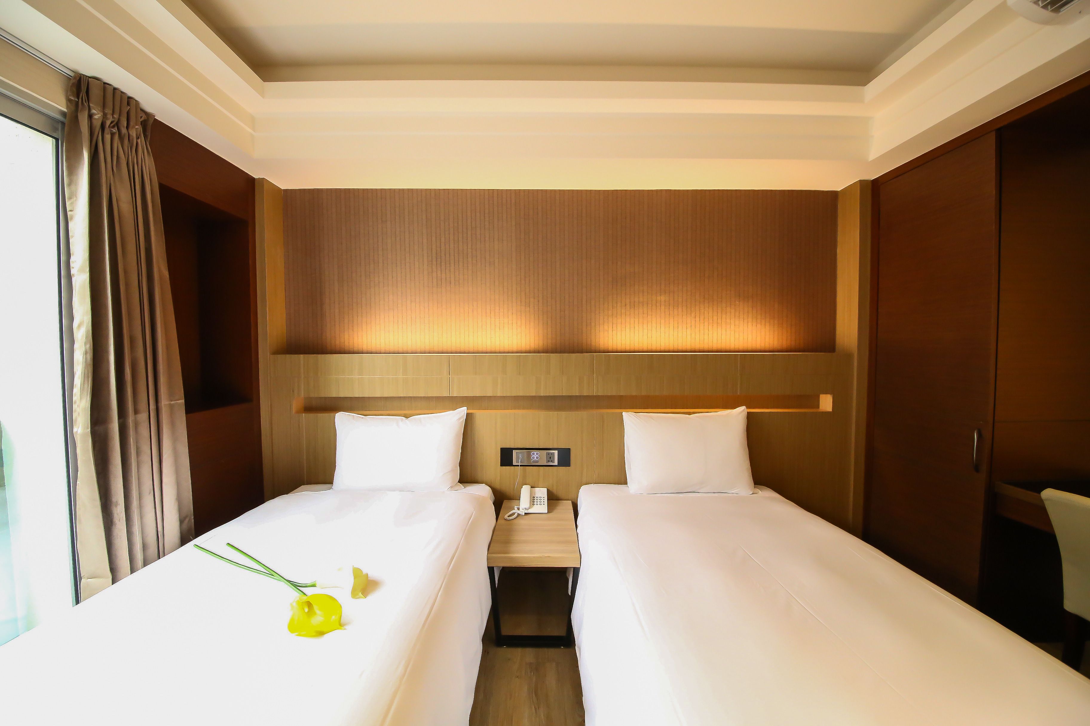 Une chambre d’hôtel avec deux lits simples, une table de chevet avec un téléphone et une tête de lit en bois.