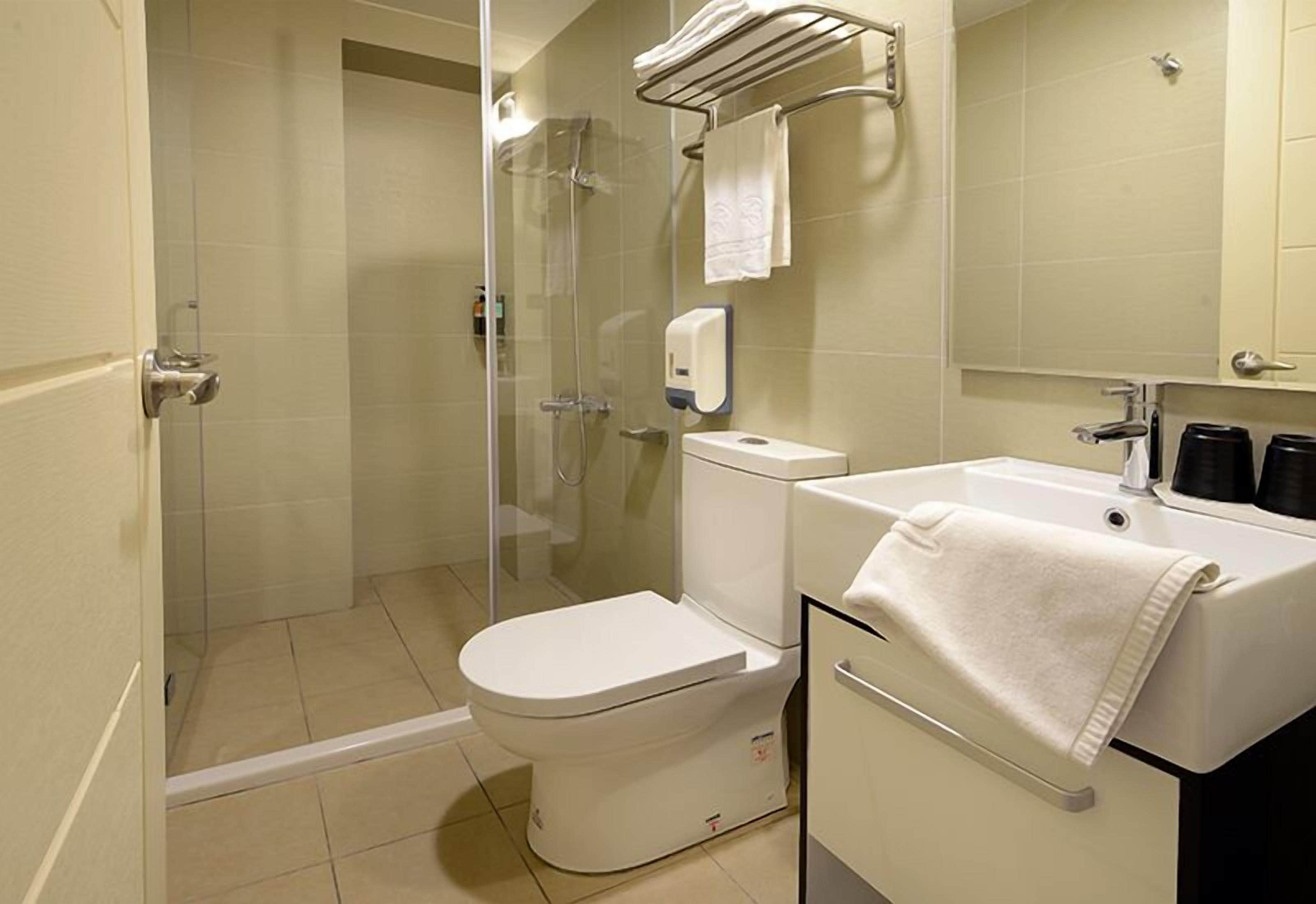 A bathroom with a toilet, a glass-enclosed shower, a sink, and a towel rack.