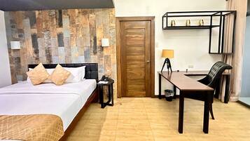 A hotel room with a bed, bedside table, lamp, desk, chair, and a wooden door.