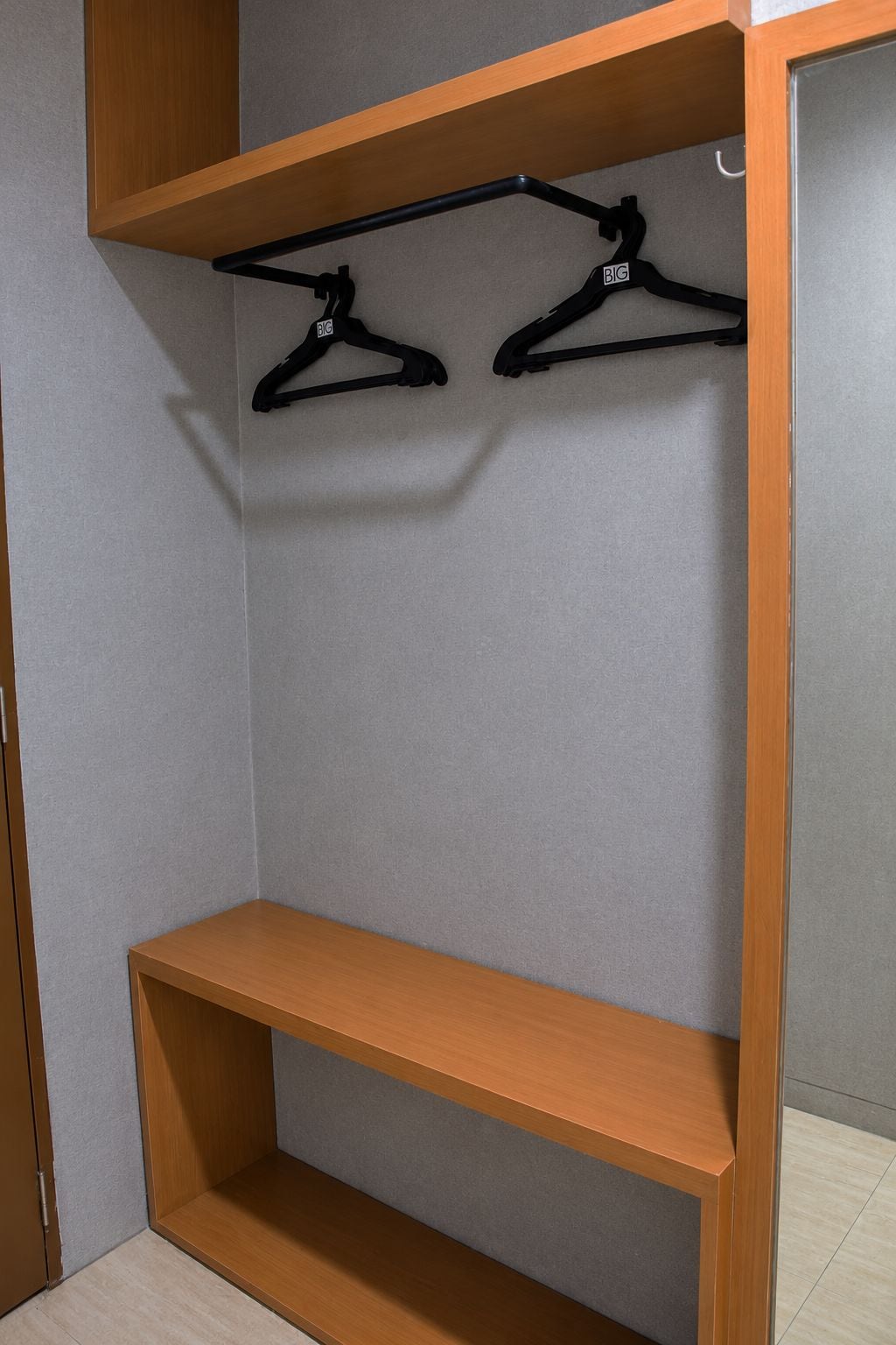A closet with wooden shelves and two black hangers.