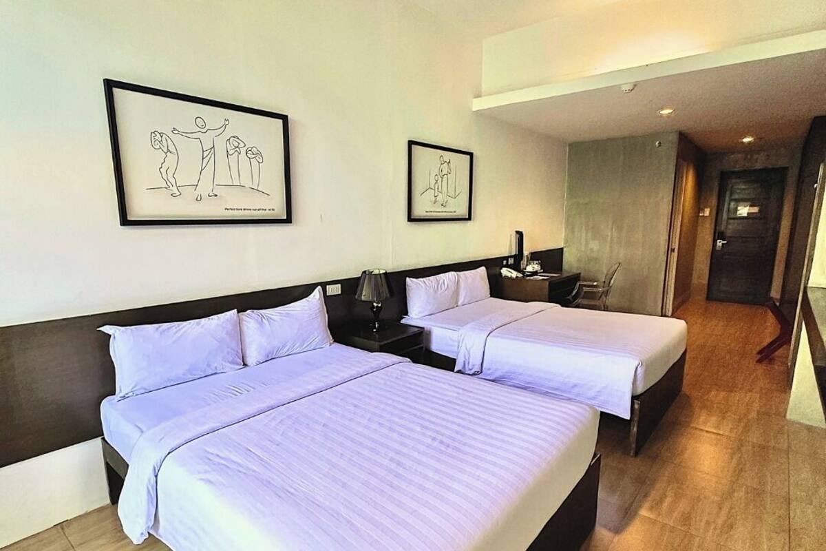 Habitación de hotel con dos camas, una mesita de noche, una lámpara y dos obras de arte enmarcadas en la pared.