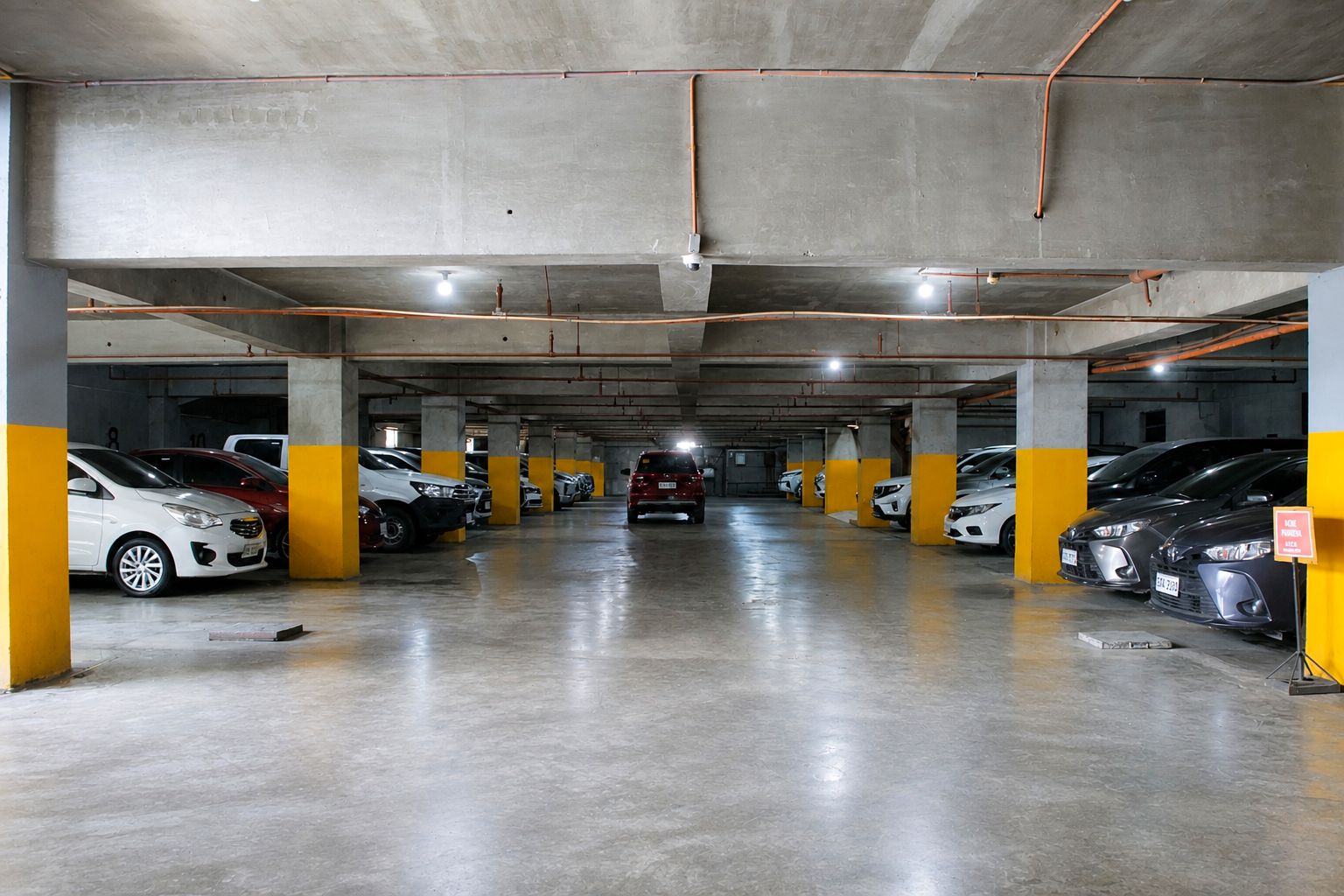 Un parking à plusieurs niveaux, avec des piliers en béton, un éclairage fluorescent et des voitures garées dans des emplacements prévus à cet effet.