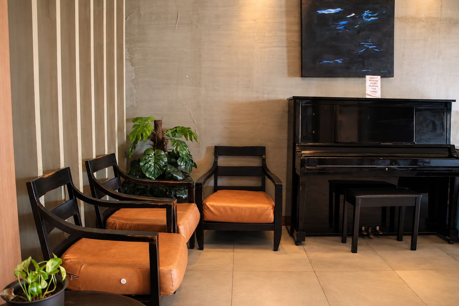 Una habitación con un piano, dos sillas con cojines naranja, una planta en maceta y una obra de arte colgada en la pared.