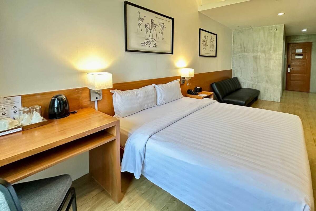 Una habitación de hotel con cama, mesitas de noche, escritorio, silla y armario.