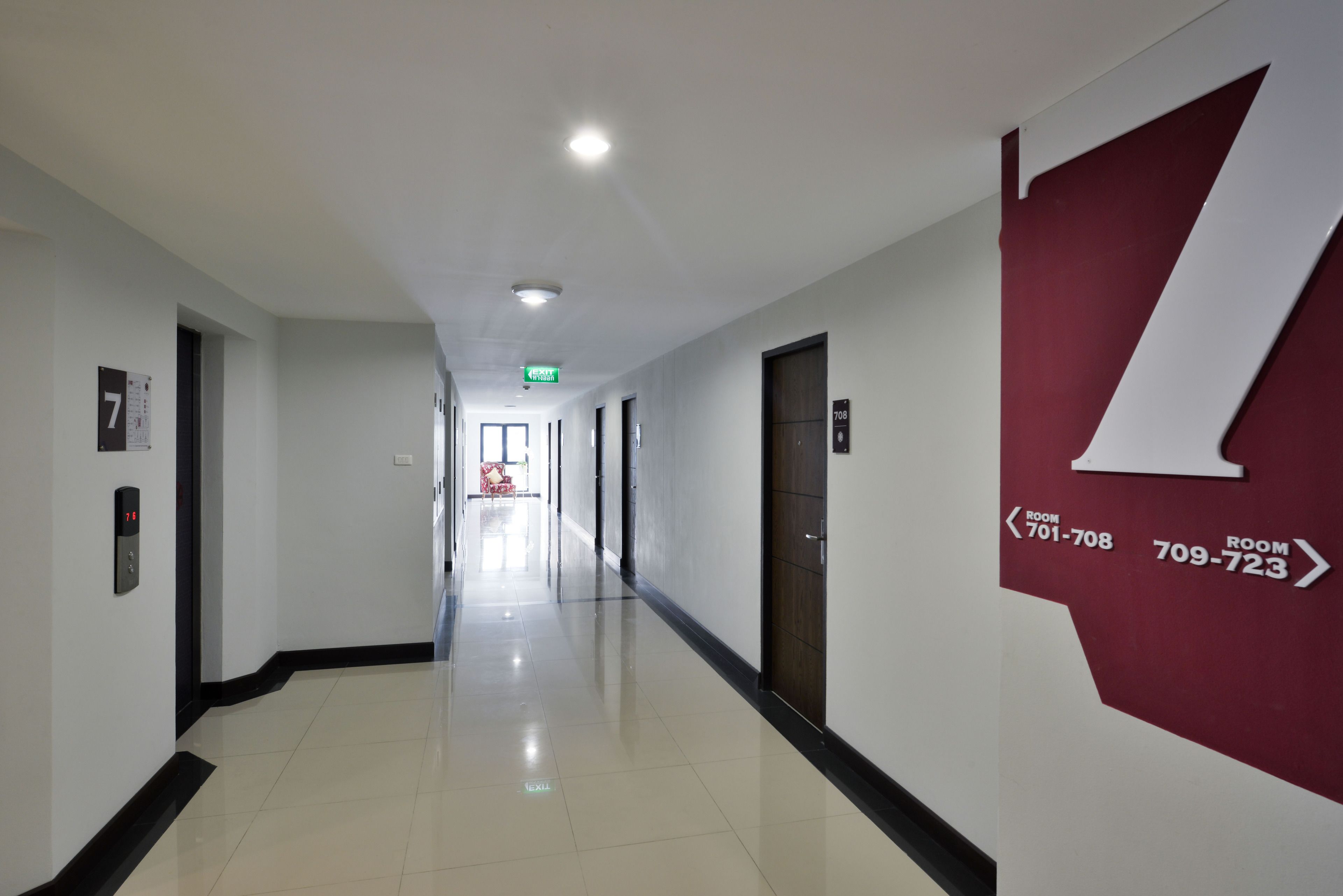 A hotel corridor with a clear floor, directional signs to rooms 701-708 and 709-723, and a red accent wall.