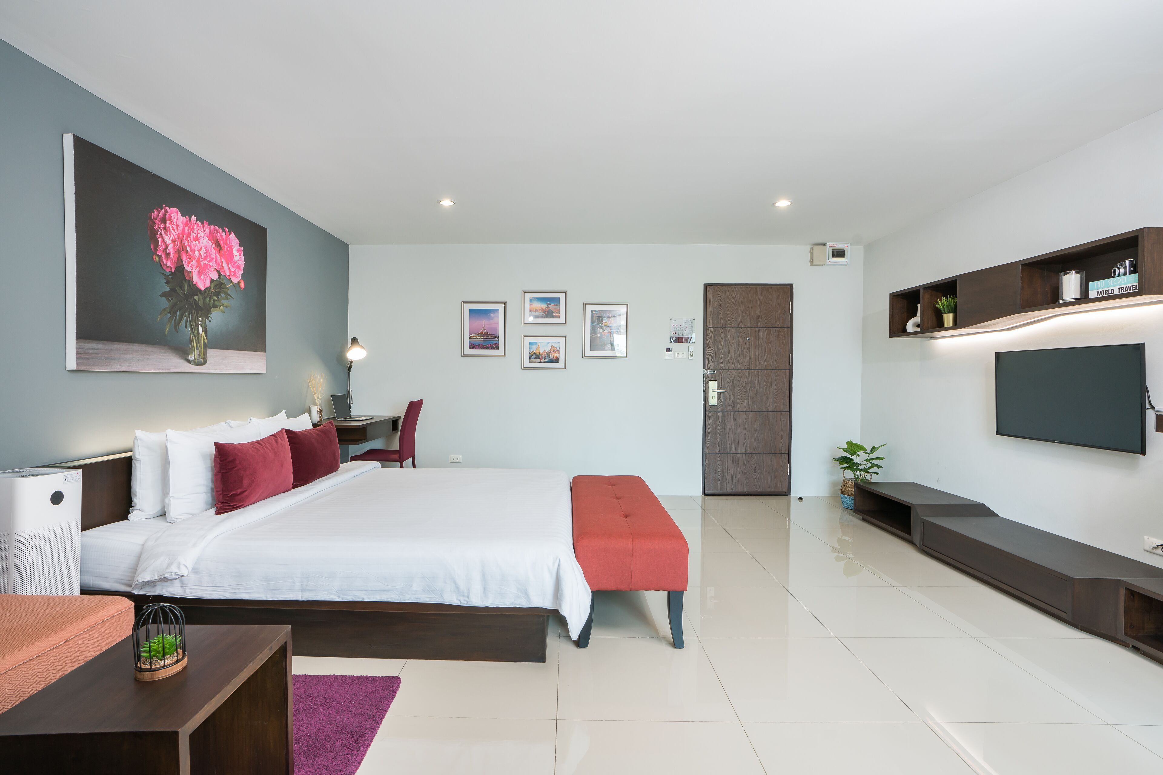 A modern bedroom with a large bed, a TV mounted on the wall, and a door leading to another room.