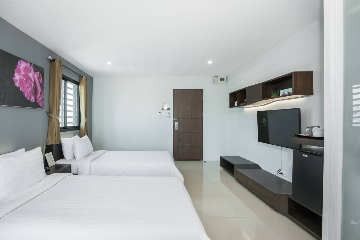 Quarto de hotel moderno com duas camas, televisão e uma kitchenette.