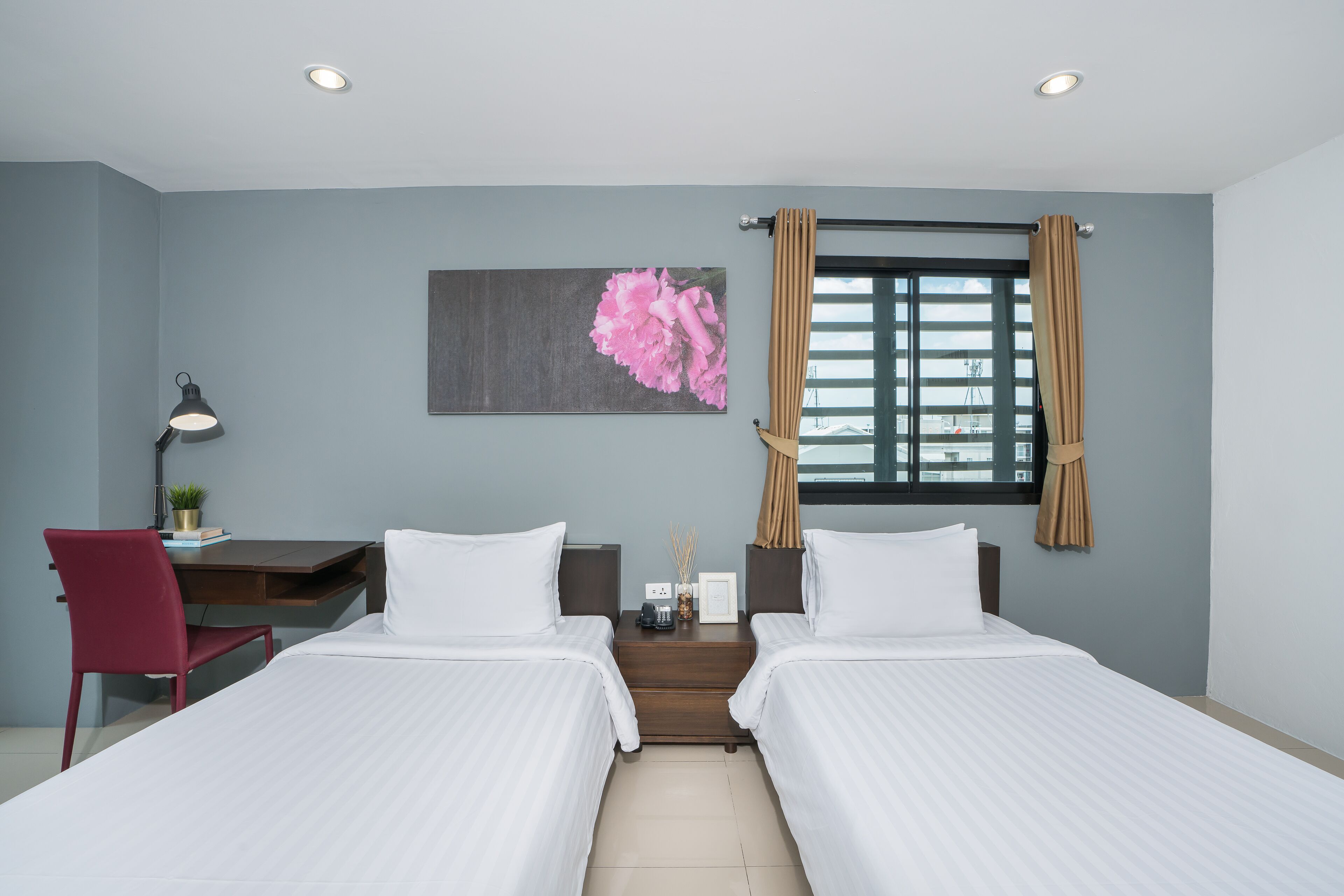 Habitación de hotel con dos camas, un escritorio, una silla, una mesita de noche y una ventana con cortinas.