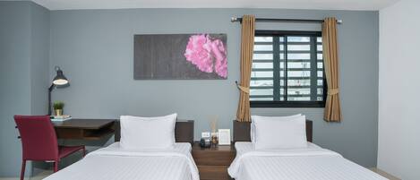 Habitación de hotel con dos camas, un escritorio, una silla, una mesita de noche y una ventana con cortinas.