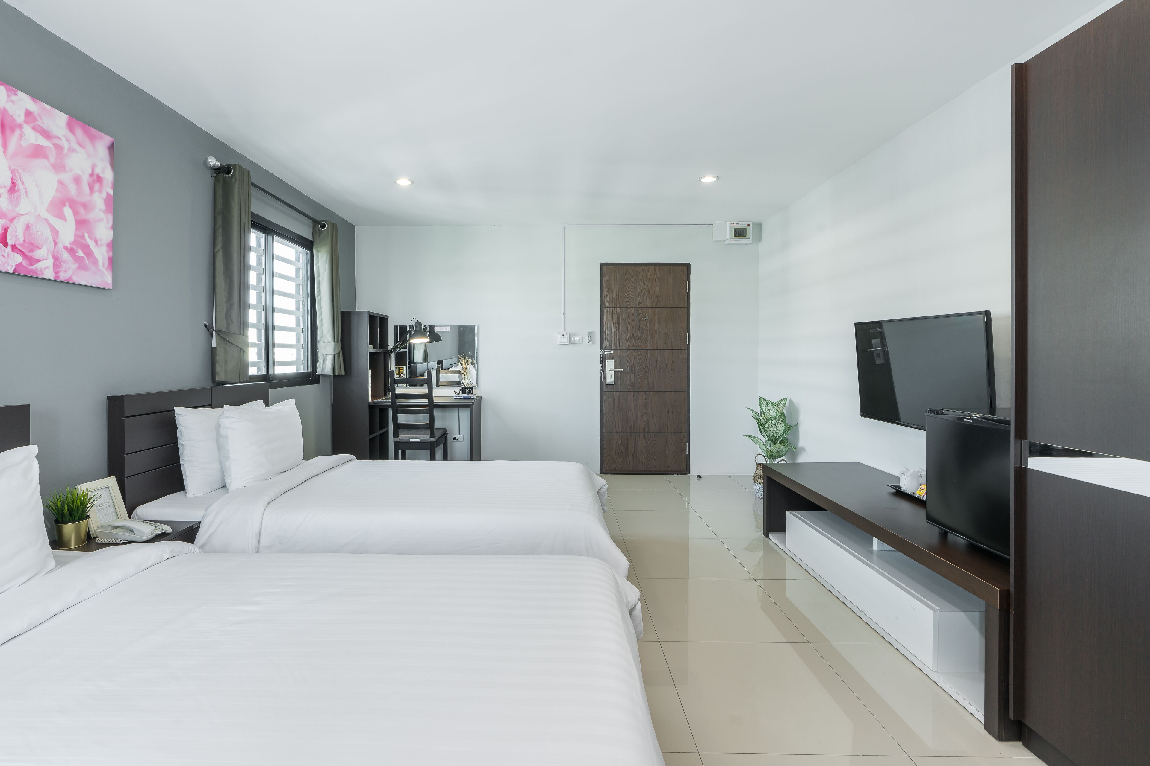 Ein modernes Hotelzimmer mit einem großen Bett, einem Schreibtisch mit Computer, einem Fernseher und einem Kleiderschrank.