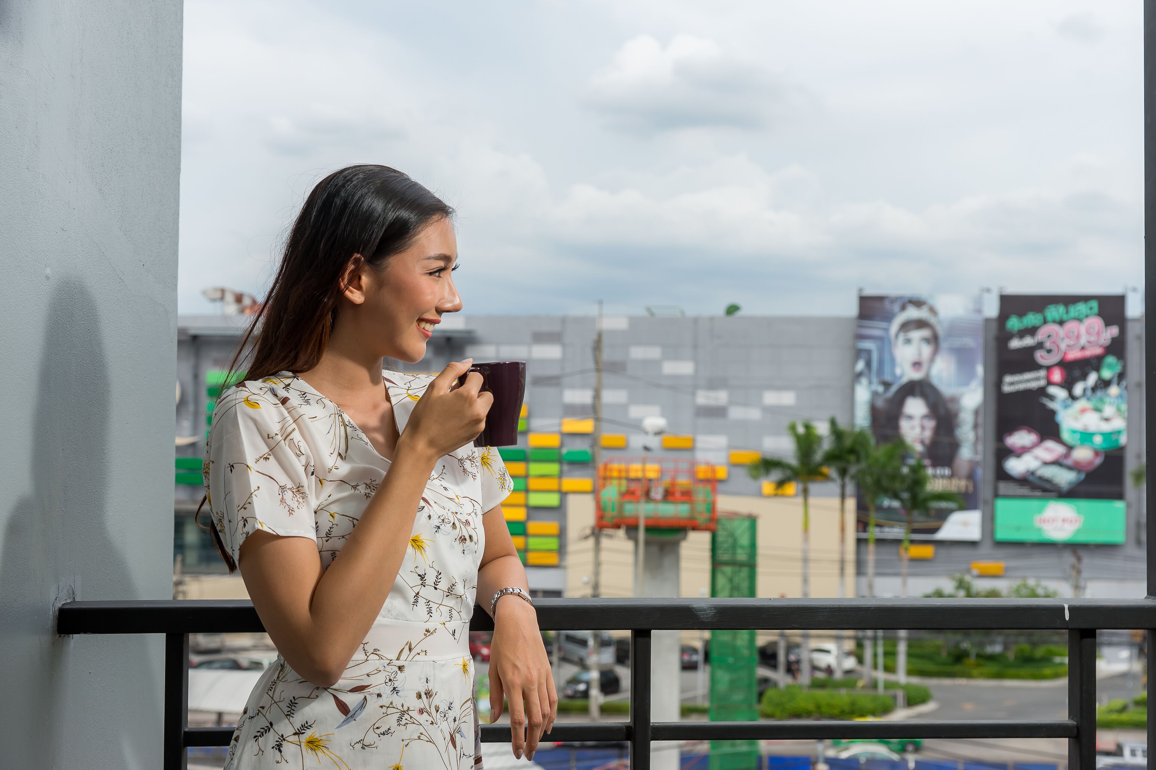 Een vrouw staat op een balkon, met een stadsgezicht op de achtergrond.