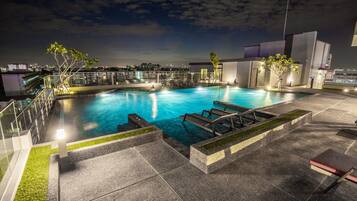 Une piscine sur le toit offrant une vue dégagée sur les gratte-ciel de la ville la nuit, entourée d’une architecture moderne et dotée de chaises longues et d’un jacuzzi.