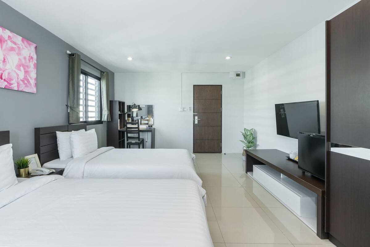 Quarto de hotel moderno com duas camas, uma escrivaninha, uma televisão e um guarda-roupa.