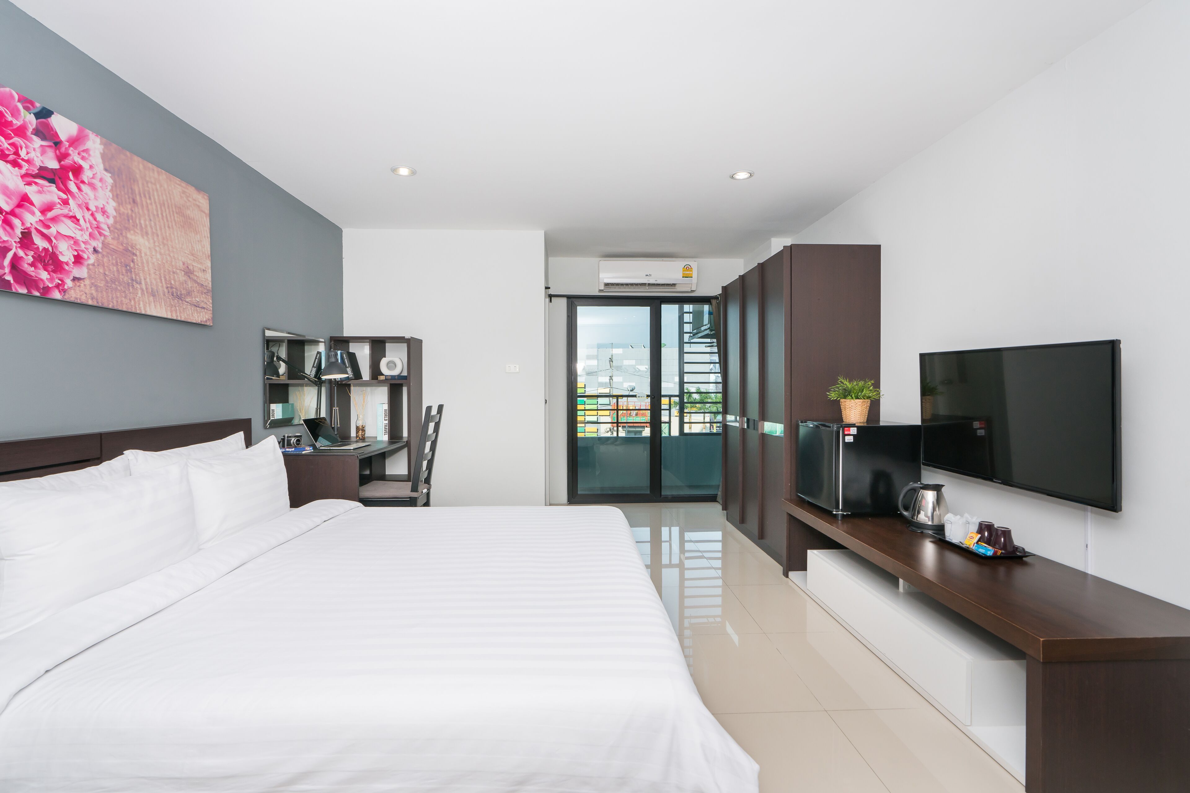 Una habitación de hotel moderna con una cama grande, un televisor de pantalla plana, un escritorio con computadora y un balcón con vistas.