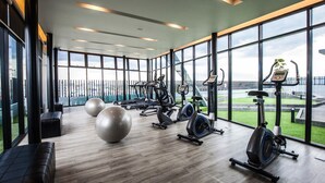 Une salle de sport moderne équipée de divers appareils d’exercice, dotée de grandes fenêtres et offrant une vue sur l’extérieur.
